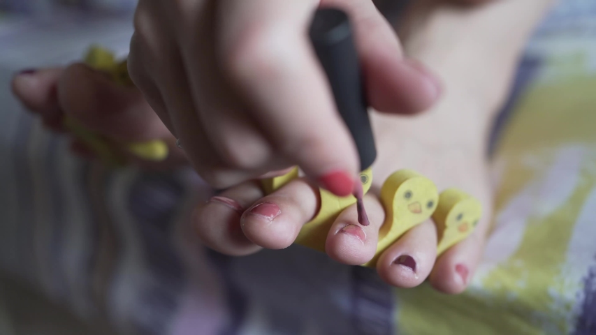 Closeup of hand painting feet nails with pink nailpolish and funny yellow ducks separating fingers, tool to separate toes