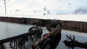 Aerial view of winter snowy sea coast with ruined boats after the shipwreck. Footage. Old sunken fishing boats on the shore of the Barents Sea.