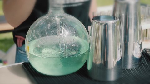 on a light background on nature the bartender pours a blue alcoholic cocktail into a flask, glass of bartender
