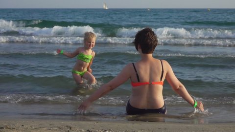 Mom and daughter are hugging each other on the seashore with their backs to the camera