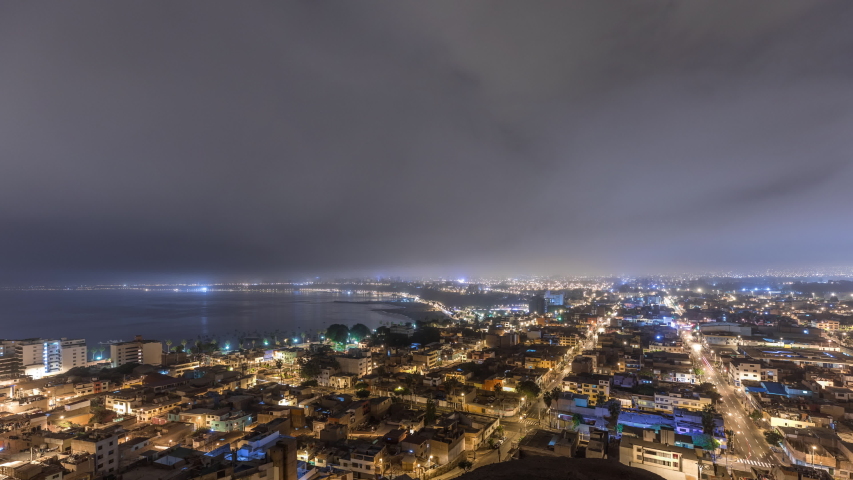 Panoramic skyline of Lima city from above with many buildings aerial night to day transition timelapse from hill. Poor houses with hills on a background. Traffic on a road near coastline. Lima, Peru