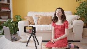 A Young Female Vlogger Recording a Video for an Online Blog with Smartphone on Tripod. The Blogger Talks and Gestures. Cozy White Home Interior with House Plants. Concept of Video Blogging.