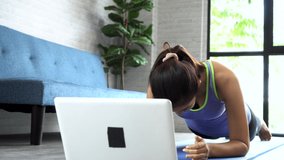 20s young Asian woman in sportswear doing plank poses while watching fitness training class on computer laptop online. Healthy girl exercising and learning in living room. Internet education concept.