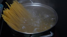 Slow motion clip of water boiling in a pot with Linguini noodles standing up.