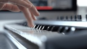 Young man in sound recording studio. Slow motion close up of guy's right hand fingers playing on keyboard. Studying or learning how to play.