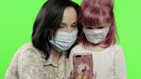 Mother, daughter wearing mask holding phone talking on video call. Social Distancing, coronavirus (covid-19) protection concept. Cute little kid enjoying using smart phone. Social media. Chroma key