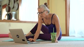 Mature woman looks at a laptop screen and then goes into the childs pose, yoga pose to stretch.
