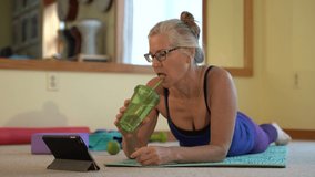 Closeup of mature woman watching online exercise instructor, drinking water and looking she is straining.