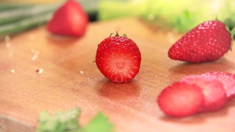 Slicing fresh strawberry on a wooden board with a large knife into slices, close up of cook hands with black gloves