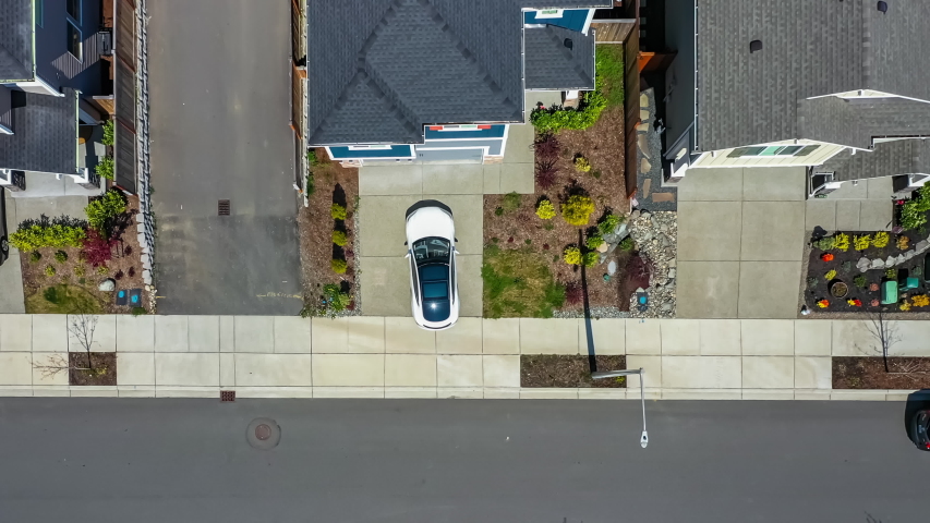 Aerial view of a white car leaving a home driveway and driving away; drone follow shot