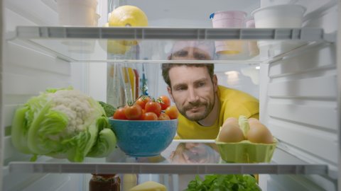 Camera Inside Kitchen Fridge: Handsome Man Opens Fridge Door, Looks inside and Disappointed Closes Door. Man Found Nothing for His Snack Time. Point of View POV Shot from Refrigerator full of Food
