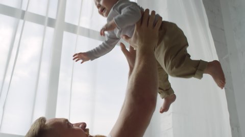 Handheld low angle shot of happy bearded father lifting adorable baby girl and smiling : vidéo de stock