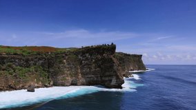 Uluwatu Hindu temple on a rock. Video shooting from a drone from the ocean. Waves break on the steep cliffs of the coast. Bukit Peninsula in Bali