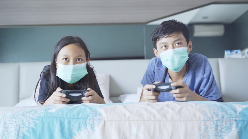 Two children playing video games while doing high five with their elbow and lying on the bed during quarantine at home. Shot in 4k resolution the bed during quarantine at home. Shot in 4k resolution