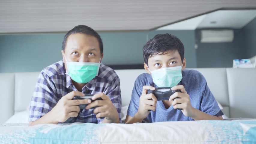 Happy father playing video games with his son while doing high five with their elbow on the bed during quarantine at home. Shot in 4k resolution