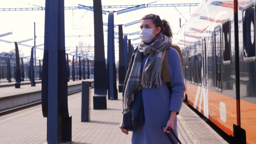 health, safety and pandemic concept - young woman in protective face mask with travel bag at railway station