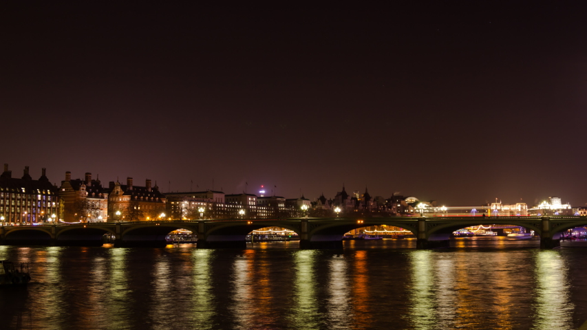 Traffic moves over Westminster Bridge and boats move underneath as the camera pans from south to north bank, revealing Parliament Royalty-Free Stock Footage #1050806089