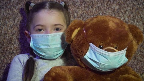 Sad kid girl with bear toy in protective medical masks at self isolation and quarantine. Stay home. Stop dangerous COVID-19 infection
