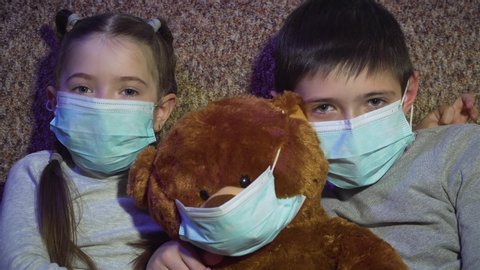 Kids with toy bear in protective medical masks sit at home in quarantine and self isolation. Stop dangerous COVID-19 infection