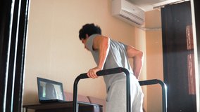 A young man conducts online training at home. Shows exercise dips shooting for web camera of the laptop. Remote work during the quarantine. - Powered by Shutterstock - Get 15% off with code: PIKWIZARD15