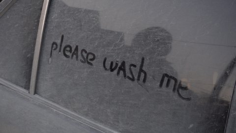 A young woman rinses off the inscription on the machine with a rag: "Please wash me." Girl washes a dirty car. Prank over the owner of the car.
