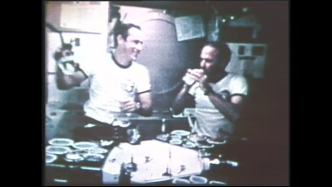 1980s: Astronauts in cabin. Men eat and drink.
