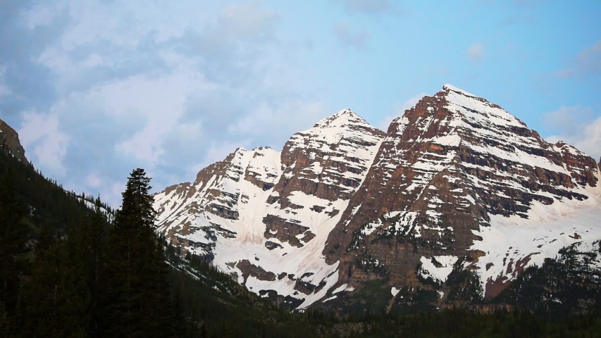 Maroon Bells peak panoramic closeup in Aspen, Colorado timelapse during blue hour dawn before sunrise with rocky mountain and snow in spring or early summer and trees clouds