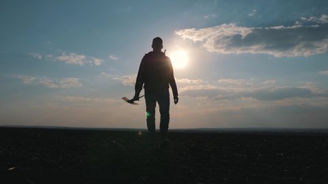Silhouette of a farmer with a shovel. Agronomist man walking on a black plowed field.