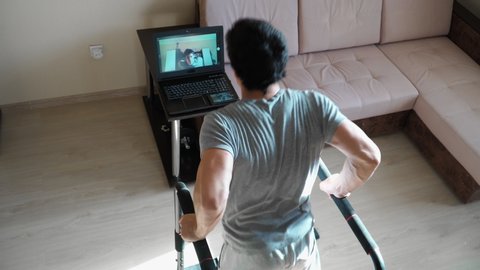A young man conducts online training at home. Shows exercise dips shooting for web camera of the laptop. Remote work during the quarantine. Top view.