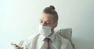 Caucasian Young Blond Hair Man Wears a White Shirt with a Tie and a Disposable Face Mask for Cough, Flu, Virus, Viral Protection. He Stays Home and Calls on his Phone in Bed because of the Quarantine