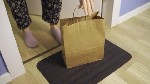 Hand with latex glove drops off package or food takeout bag - woman picks it up - package left at door front in coronavirus times - order food - no contact delivery, contactless