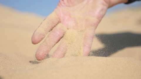 Exciting view of a young male hand plunging with its fingers in hot sand, raising it up and sieving it in the desert on a sunny day in spring in slow motion.