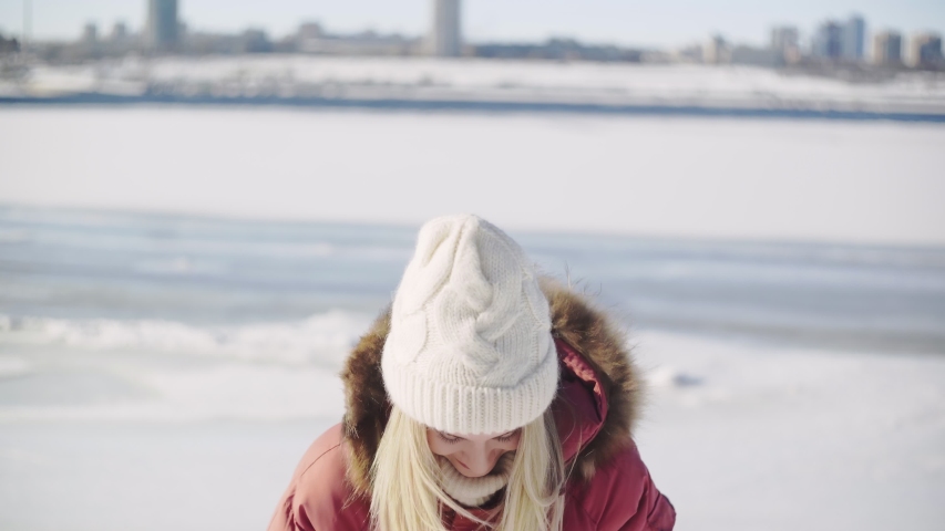 Young woman in white knitted hat and red winter jacket posing with two mandarins on the camera