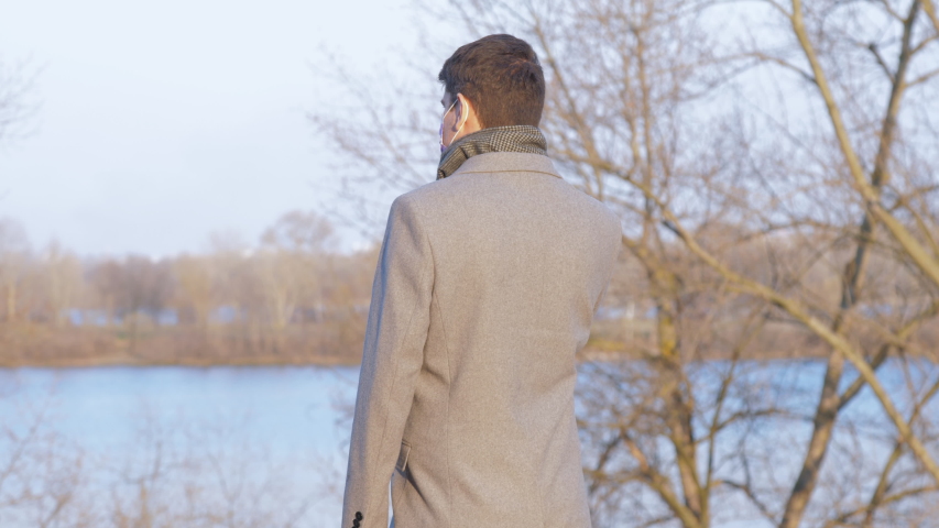 gentleman has conversation on device with mask protecting from illness and turns back against sunshine slow motion. Concept pandemic coronavirus environment