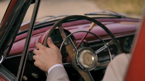 Man driving red retro car. Close up of male hands holding the steering wheel of a vintage car. Young guy inside his old red automobile. Man holding hands on a steering wheel and drives a retro car.