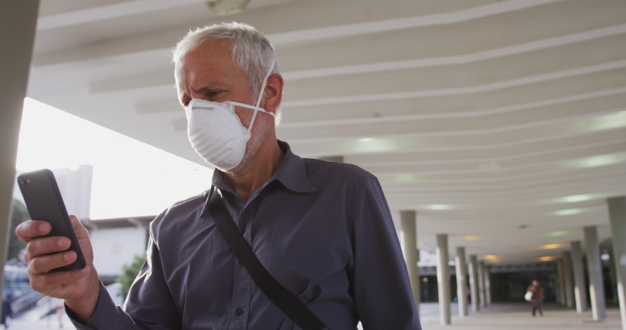Middle aged Caucasian man out and about in the city streets during the day, wearing a face mask against coronavirus, covid 19 and using his smartphone, in slow motion. Royalty-Free Stock Footage #1050866626