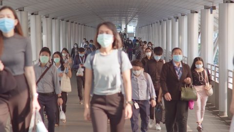 Bangkok, Thailand - Apr 7, 2020: Crowded Asian people wear face mask walking in pedestrian walkway. Coronavirus disease Covid-19 pandemic outbreak, city life, or air pollution concept. 4K slow motion