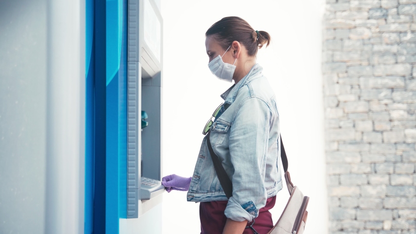 A young woman in a medical mask and protective latex gloves using an ATM machine to get money from her credit card. Coronavirus COVID-19 pandemic conditions. Royalty-Free Stock Footage #1050873676