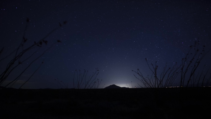 Time lapse of stars moving over a distant mountain backlit by city glow