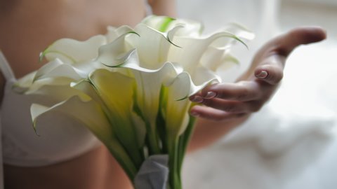 Bride's morning. Bride in lingerie and   veil holding her wedding bouquet of white callas. Close up of female hands holding wedding bouquet of white callas.
