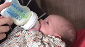 4K: Mother feeding Milk to her baby with a bottle. They are indoors, The newborn is sat in her mum's arms. Stock Video Clip Footage