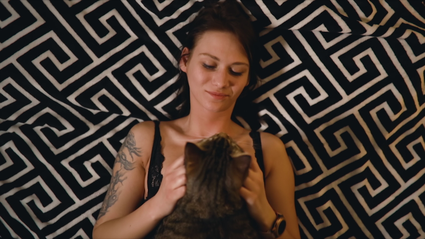 Brunette woman rests on bed with cat sitting on top