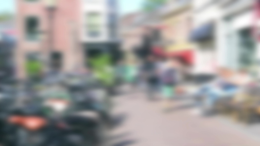 Abstract blurred people walking down an urban street in sunshine with parked bicycles on one side and cafe at the other.