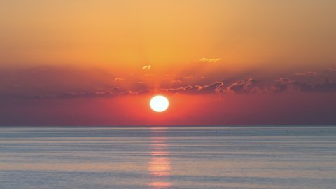 Sunrise over calm sea. Dawn over horizon, ocean, water - timelapse or hyperlapse. Red cloudy sky. Solar path on water