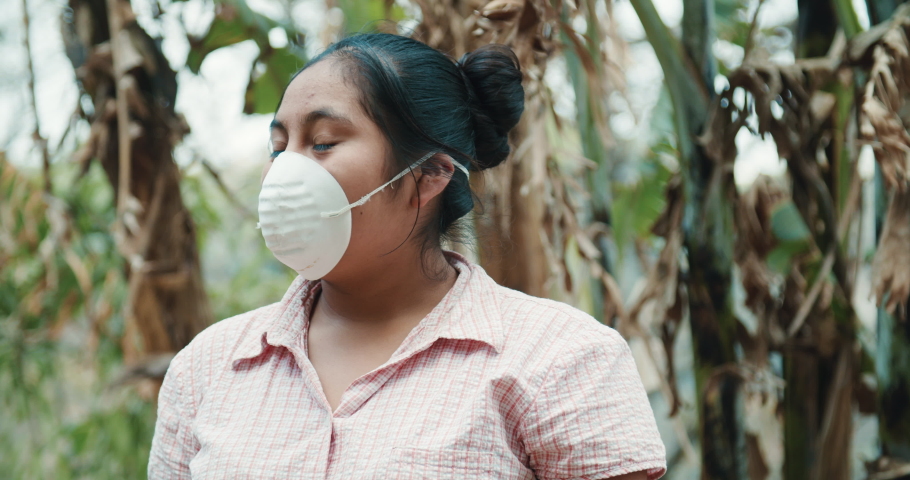 close up of a friendly young hispanic teen wearing a protective face mask while working on a rural village surrounded by agriculture and nature during coronavirus outbreak.  Royalty-Free Stock Footage #1050920149