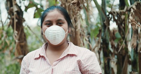 close up of a friendly young hispanic teen wearing a protective face mask while working on a rural village surrounded by agriculture and nature during coronavirus outbreak. 