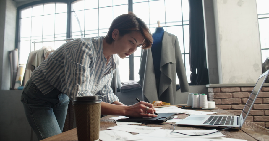 A hipster female clothing designer is redrawing her sketches on graphics tablet, designing her new collection - fashion, small business concept 4k footage