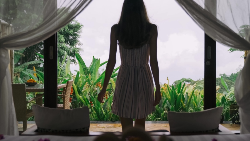 Happy slim fit girl in light dress with brown hairstyle and a good figure go from hotel room to terrace with nice view of tropic forest, jungle view. Stretching Arms Back Rear View. 4k.