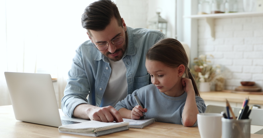 Young father checking homework helping cute school child daughter with studies sit at kitchen table. Adult parent or tutor explaining kid girl distance learning at home. Private education concept Royalty-Free Stock Footage #1050934606