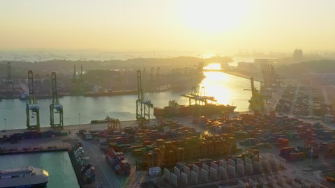 Cargo container transport ship and crane at Singapore sea port industrial district, silhouette sunset. Logistic industry, freight transportation business concept. Drone aerial high angle view panning